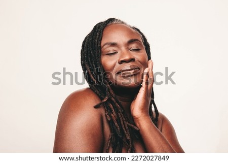Beautiful woman with dreadlocks touching her flawless skin with her eyes closed. Confident dark-skinned woman embracing her smooth melanated skin. Mature black woman ageing gracefully.