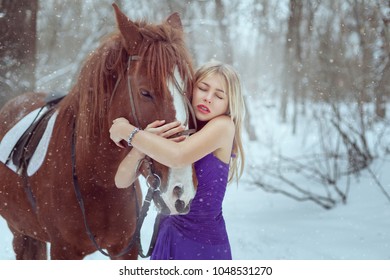 Beautiful woman in a dress hugging a horse. They stand in a winter park, it's snowing