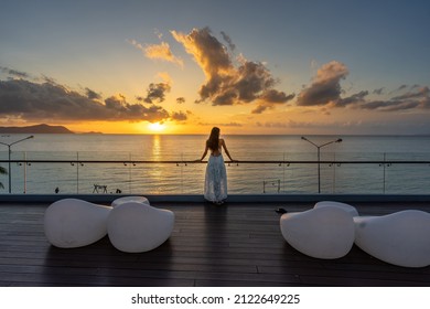 Beautiful woman in dress standing and enjoying the large balcony on sunset with sea view. Back view