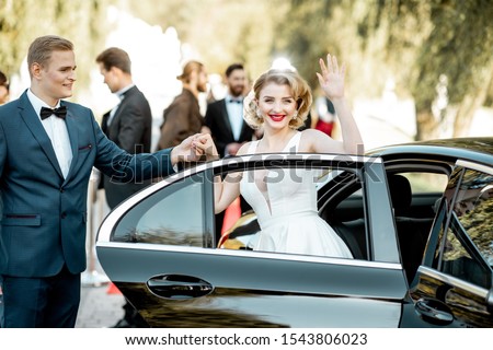 Beautiful woman dressed in retro style as a famous movie actress arriving on the awards ceremony with man helping to get out of the car