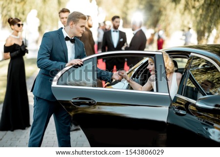 Beautiful woman dressed in retro style as a famous movie actress arriving on the awards ceremony with man helping to get out of the car