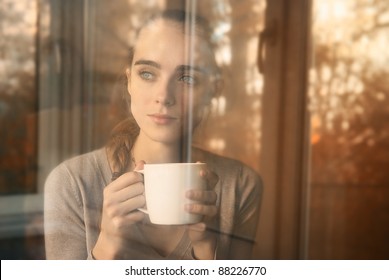 beautiful woman drinking coffee in the morning sitting by the window. view from outside.