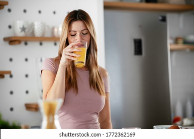 Beautiful woman drinking orange juice in the kitchen. Young woman reading the news online.
