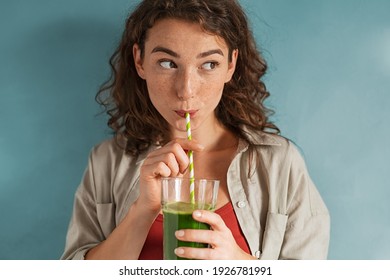 Beautiful woman drinking an organic green smoothie. Fit young woman drinking detox juice using paper straw isolated against blue background. Healthy girl enjoy detox drink and looking away.  - Shutterstock ID 1926781991