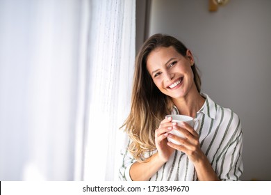 beautiful woman drinkink coffee inside her home next to the bright window, enjoying the moment and the tast of the drink, looking outside. rest at home