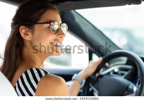 Beautiful woman driving. Beautiful\
smiling woman driving her car and looking into right side\
mirror