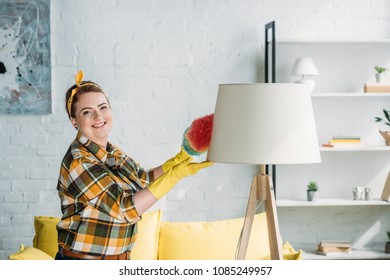 Beautiful Woman Dusting Lamp With Dust Brush At Home