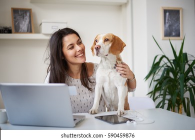 Beautiful woman in early thirties working from home. Dog helps her