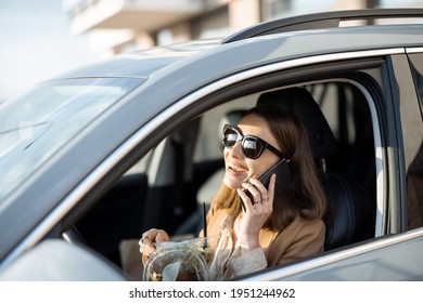 Beautiful Woman Eating Heathy Salad In The Car And Speaking On The Phone. Received A Food Order To Go. Have A Quickly Snack On The Lunch Break. 