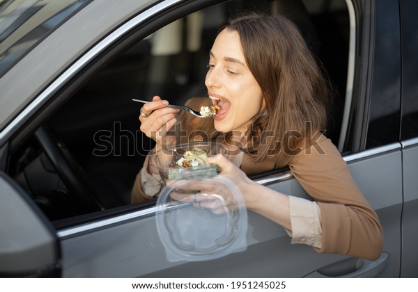 Beautiful woman\
eating heathy salad in the car. Received a food order to go. Have a\
quickly snack on the Lunch Break.\
