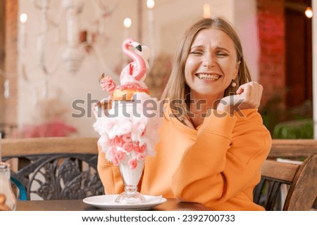 Beautiful woman eats dessert in form pink flamingo in cafe. Time for fun, vows in a bright sweatshirt