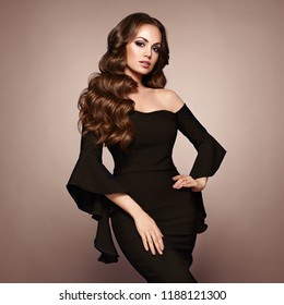 Beautiful woman in elegant black evening dress. Brunette Girl with Long Healthy and Shiny Curly Hair. Care and Beauty. Beautiful Model Woman with Wavy Hairstyle