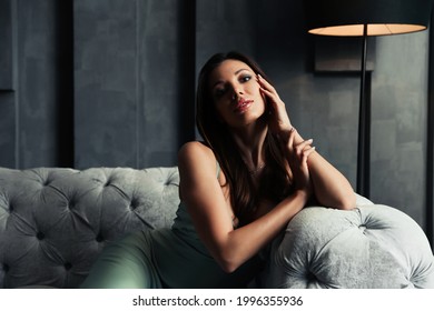 Beautiful Woman In Elegant Dress On Sofa Indoors. Luxury Lifestyle