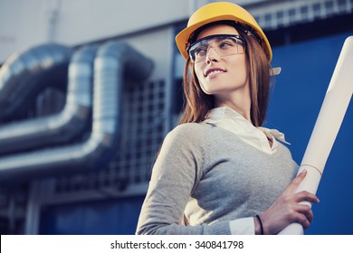 Beautiful Woman Engineer Is Standing In Front Of An Industrial Pipes Background