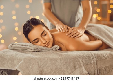 Beautiful woman enjoying body massage at a spa salon. Relaxed young girl lying on a massage table while a professional masseuse is massaging her back. Beauty, health, pleasure, pampering concept - Powered by Shutterstock