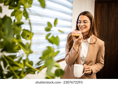 Beautiful woman enjoying the moment and eating delicious donuts at work.