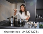 Beautiful woman enjoying perfect food, bellissimo hand sign, testing the tomato pasta sauce for taste, cooking dinner in the gray color minimalist home kitchen interior.