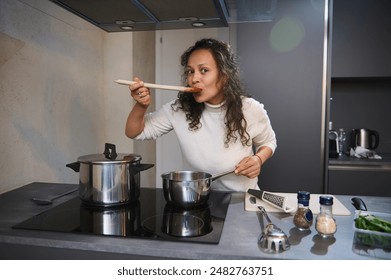 Beautiful woman enjoying perfect food, bellissimo hand sign, testing the tomato pasta sauce for taste, cooking dinner in the gray color minimalist home kitchen interior. - Powered by Shutterstock