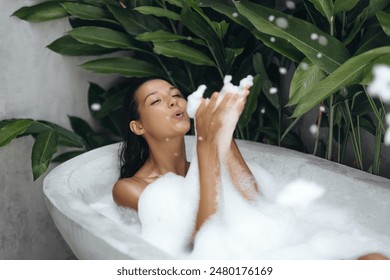 A beautiful woman enjoys a playful bubble bath in a tropical outdoor setting, surrounded by lush greenery. Ideal for concepts of relaxation, luxury, and spa lifestyle in advertisements and promotional - Powered by Shutterstock