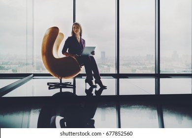 Beautiful woman entrepreneur is sitting alone with laptop on modern yellow curved armchair in office interior with reflections on high floor of skyscraper with copy space place for logo or your text - Powered by Shutterstock