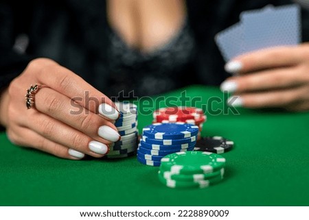 beautiful woman in an evening black dress plays poker in a casino at a green table. Takes a bet on all chips. poker is a game of chance.