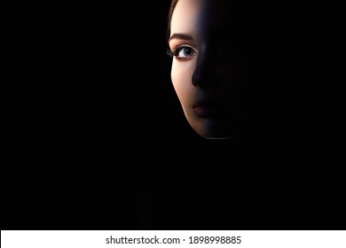 beautiful woman eye, looking from the dark. pretty young woman face part. hide and seek