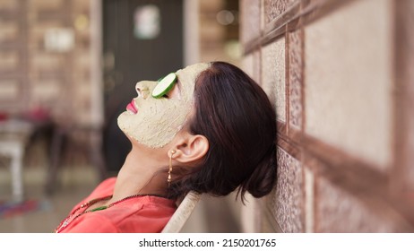 A beautiful woman with facial clay mask on face and fresh cucumber on eyes relaxing at Home. Portrait of beautiful spa girl. Beauty, healthcare. Multani Mitti and green Face Pack in India - Powered by Shutterstock