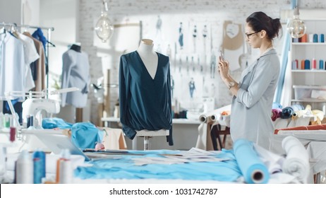 Beautiful Woman fashion, designer,  Working with Tailoring Mannequin, Adjusting Blouse, Using Smartphone. Her Studio is Bright and Sunny, Clothes Hanging, Colorful Fabrics Lying on the Table. - Powered by Shutterstock