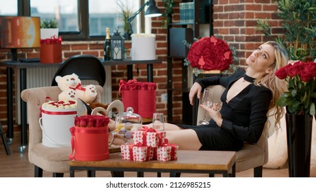 Beautiful Woman Feeling Lonely Lying With Feet Up With Empty Glass Of Champagne Waiting For Love One Being Late. Sad Seductive Woman Is Dissapointed In Room Full Of Valentine Day Luxury Gifts.