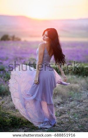 Beautiful woman in a field of lavender on sunset. Woman in amazing dress walk on the lavender field.
