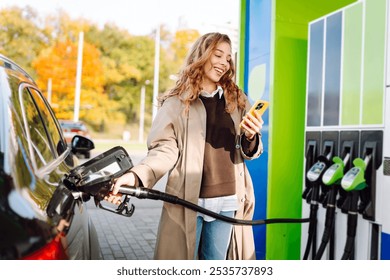 Beautiful woman filling her car with gasoline at the gas station. Online pay. Woman pays for a gas station using an app on her phone.