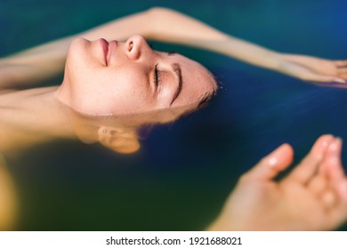 Beautiful Woman Floating In Tank Filled With Dense Salt Water Used In Meditation, Therapy, And Alternative Medicine. 
