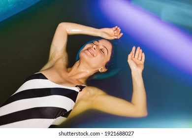 Beautiful Woman Floating In Tank Filled With Dense Salt Water Used In Meditation, Therapy, And Alternative Medicine. 
