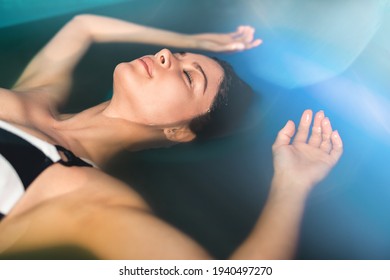 Beautiful woman floating in tank filled with dense salt water used in meditation, therapy, and alternative medicine. 