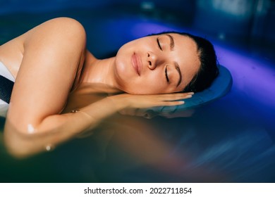 Beautiful Woman Floating In Tank Filled With Dense Salt Water Used In Meditation, Therapy, And Alternative Medicine. 
