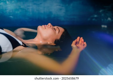 Beautiful woman floating in tank filled with dense salt water used in meditation, therapy, and alternative medicine. 