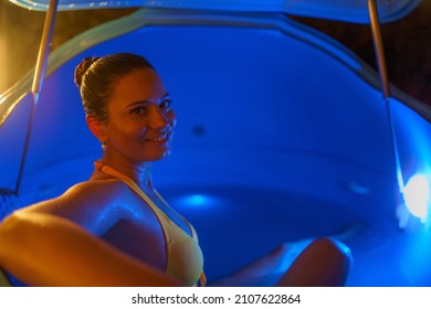 Beautiful Woman Floating In Tank Filled With Dense Salt Water Used In Medical Therapy, Looking At Camera.