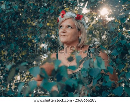 Beautiful woman with flower crown pose for camera. A young woman was hiding behind the birch branches