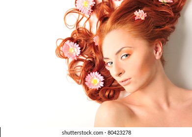 Beautiful woman with flowers in her red hair she is lying relaxed on white background