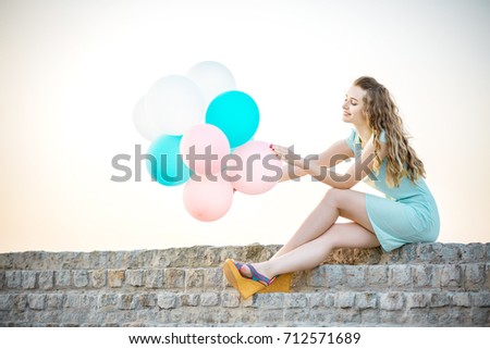  beautiful woman with flying multicolored balloons sitting and dreaming against the sky. soft light