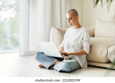 Beautiful Woman Freelancer With Very Short Hair Works, Checks Email And Social Networks  While Sitting On Floor  Near Sofa  And Working On Laptop During Work From Home In Daytime
