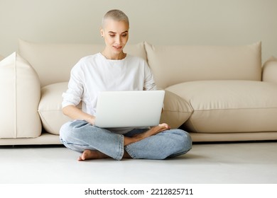 Beautiful Woman Freelancer With Very Short Hair Works, Checks Email And Social Networks  While Sitting On Floor  Near Sofa  And Working On Laptop During Work From Home In Daytime
