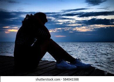 Beautiful woman in frustrated depression sitting on wooden bridge, near the beach on sunset. Concept of Major depressive disorder, unemployed, sadness, depressed and human problems in dark tone.