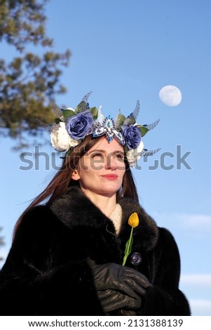 Beautiful woman in fur coat and Gothic headdress poses against the sky.