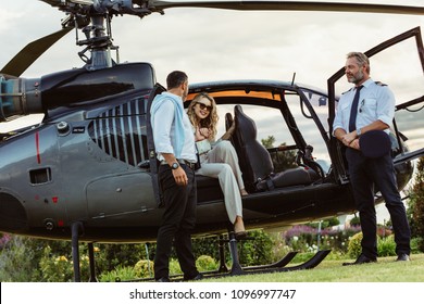Beautiful woman getting down the helicopter with the help from her boyfriend. Couple disembarking their helicopter with pilot standing by.