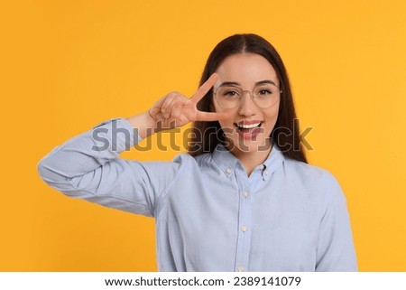 Beautiful woman in glasses showing V-sign on orange background