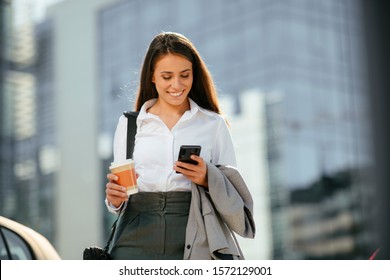 Beautiful Woman Going To Work With Coffee Walking Near Office Building. Portrait Of Successful Business Woman Holding Cup Of Hot Drink.