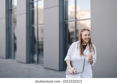 Beautiful woman going to work with ice latte walking near office building. Successful business blonde girl holding cup of hot drink, laptop, phone on her way to work on city street. High resolution. - Powered by Shutterstock