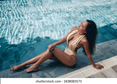 beautiful woman in golden bikini sitting near swimming pool, summer vacation.