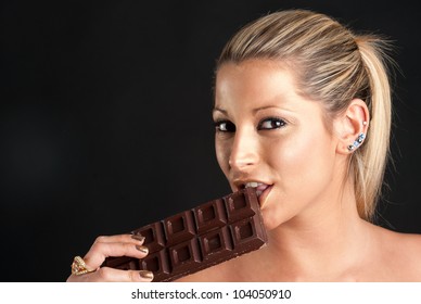 Beautiful Woman With Golden Make Up Eating Chocolate Against Black Background.